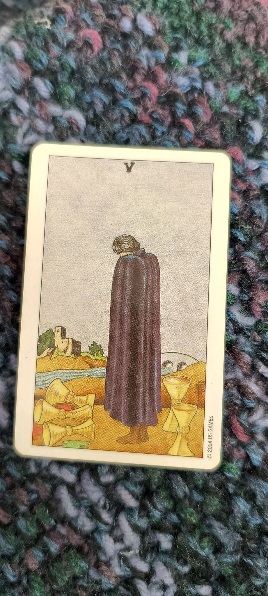 A caped figure looks sadly at three cups that have spilled, while behind the figure are two more cups that have not spilled.